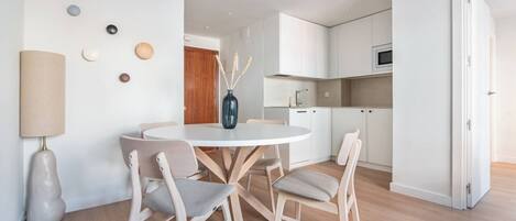 Una cocina moderna con armarios blancos, un microondas y un comedor con una mesa redonda y cuatro sillas.