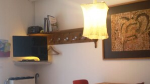 Ein Zimmer mit einem Bett, einem Schreibtisch mit zwei roten Stühlen, einem Fernseher, einer Lampe und einem gerahmten Bild an der Wand.