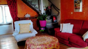 A living room with a wooden floor, a red sofa, a white armchair, and a small round table with a pink pot.