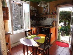 A small kitchen with a dining table, chairs, and a window overlooking a stone wall. - House 2 pers Volvic parc des Volcans, shady garden. Comfortable 70 m² . (Volvic)