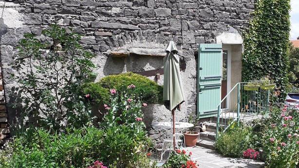 A stone building with a garden entrance, a small door, and a covered area with a table and chairs.