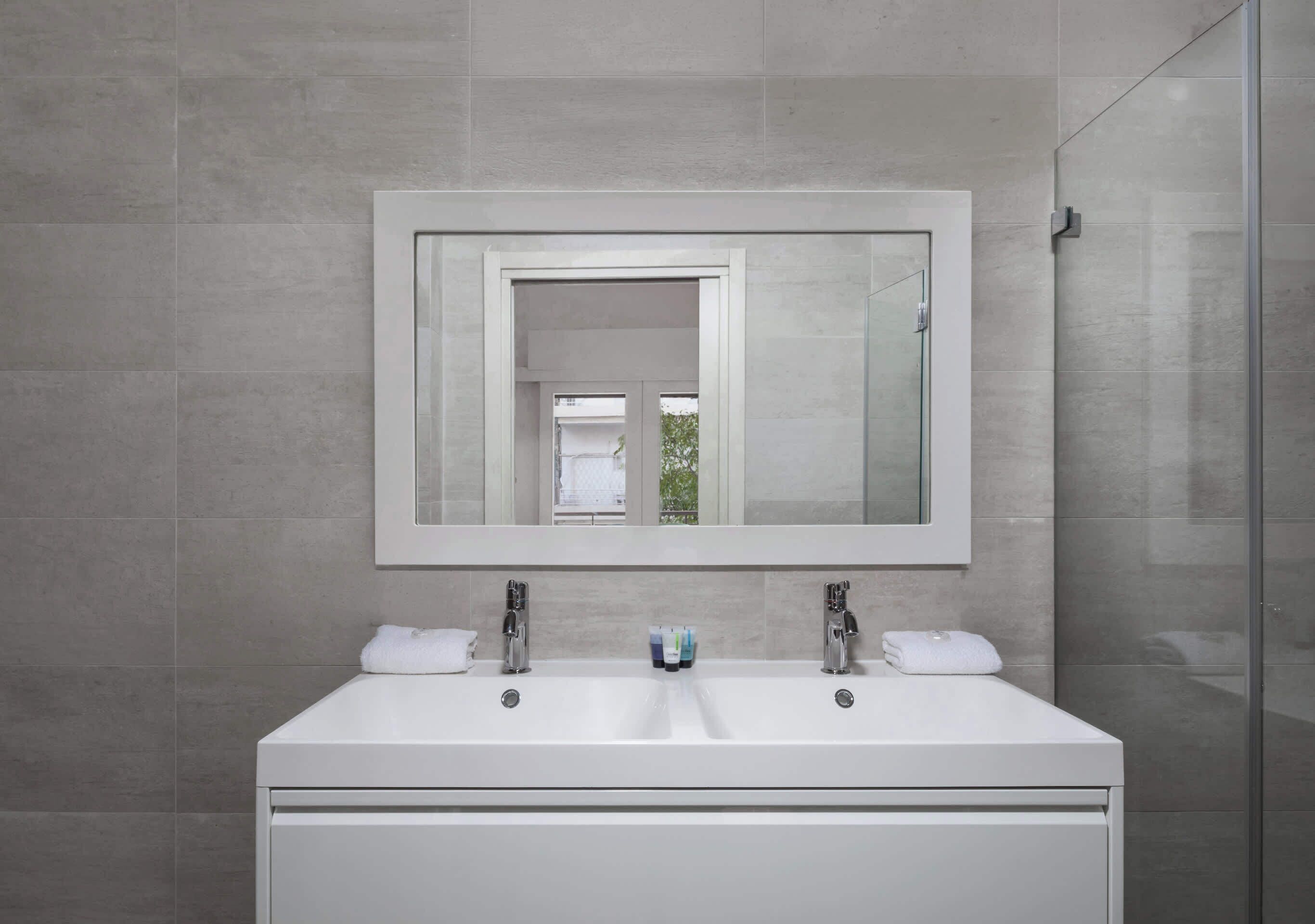 A modern bathroom with a large mirror, two sinks, and a glass shower enclosure.