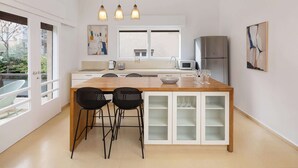 A modern kitchen with a wooden island, two black chairs, a stainless steel refrigerator, and pendant lights. - Peaceful 2BR Apt w/ Balcony by HolyGuest (Tel Aviv-Yafo)