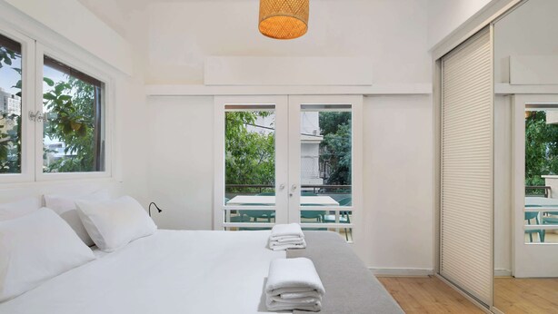 A modern hotel room with a large bed, a hanging light fixture, and a balcony with outdoor seating. - Peaceful 2BR Apt w/ Balcony by HolyGuest (Tel Aviv-Yafo)