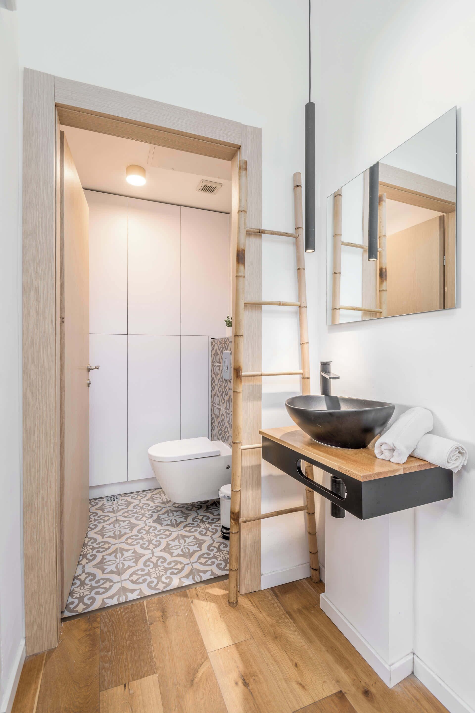 Une salle de bain au design moderne, avec un plancher en bois, des toilettes blanches, un lavabo noir et un miroir au-dessus du lavabo.