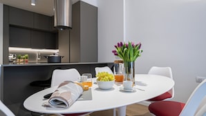A modern dining area with a white table, red chairs, a bowl of grapes, a glass of orange juice, and a vase with flowers. - Italianway Comfort - Vincenzo Monti 29 F (Milan)