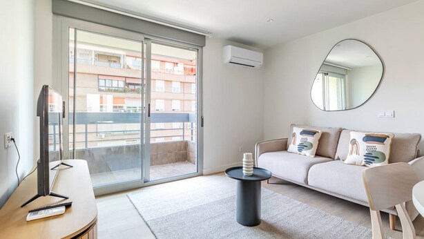 Un soggiorno moderno con un divano, un tavolino da caffè, una televisione e una porta vetrata scorrevole che dà su un balcone.