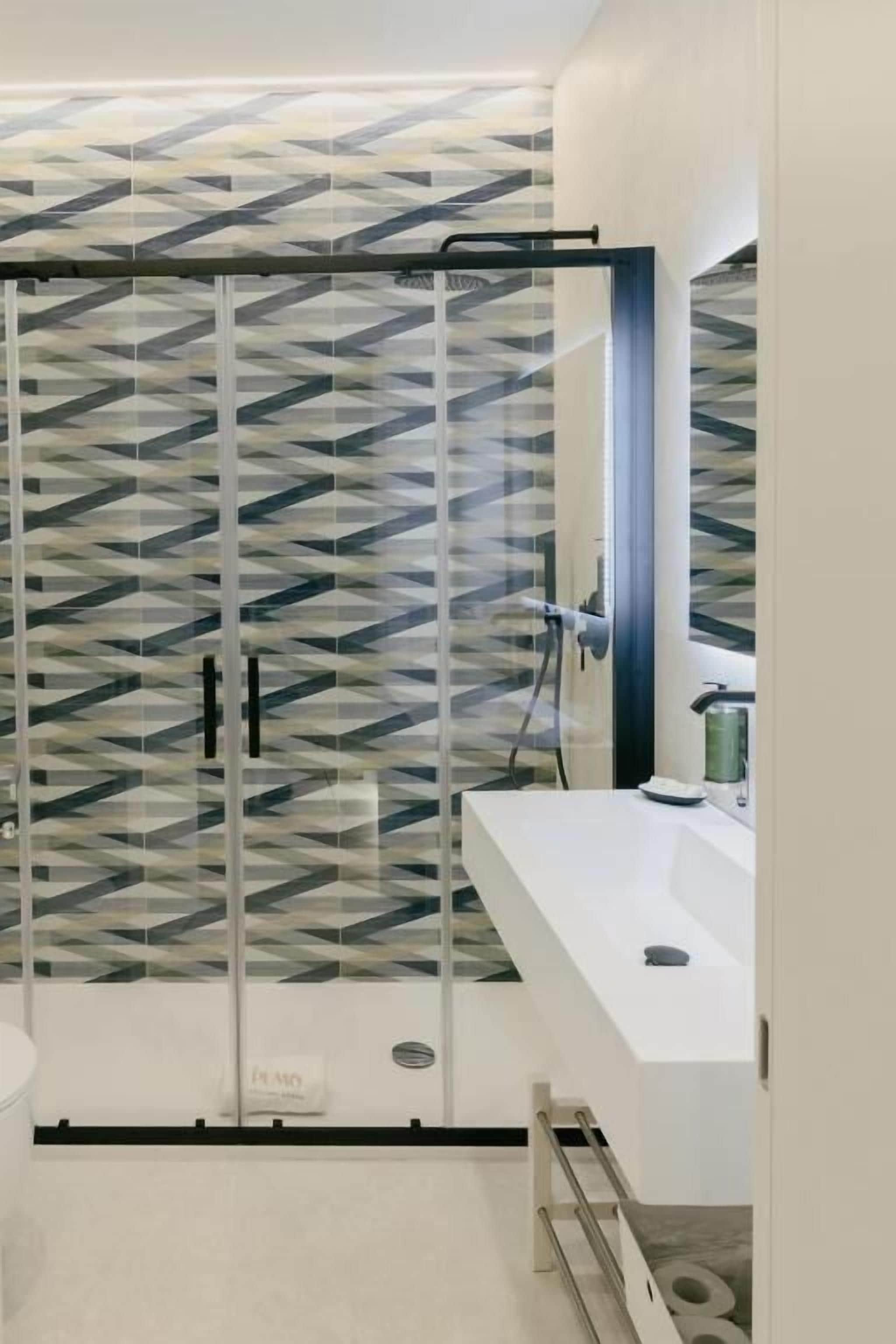 A modern bathroom with a geometric patterned shower enclosure, a white sink, and a mirror.