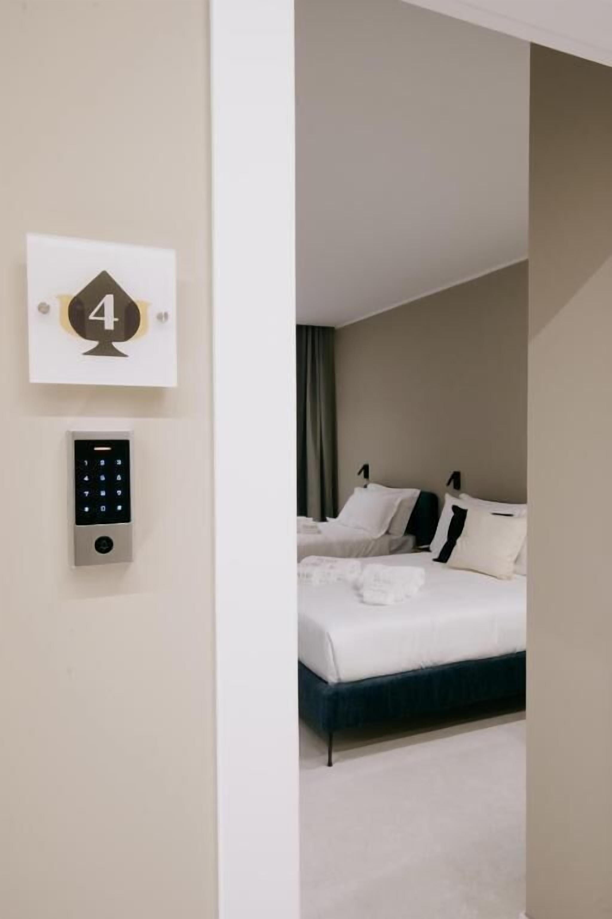 Una habitación de hotel con cama, panel de control en la pared y una puerta con un número.