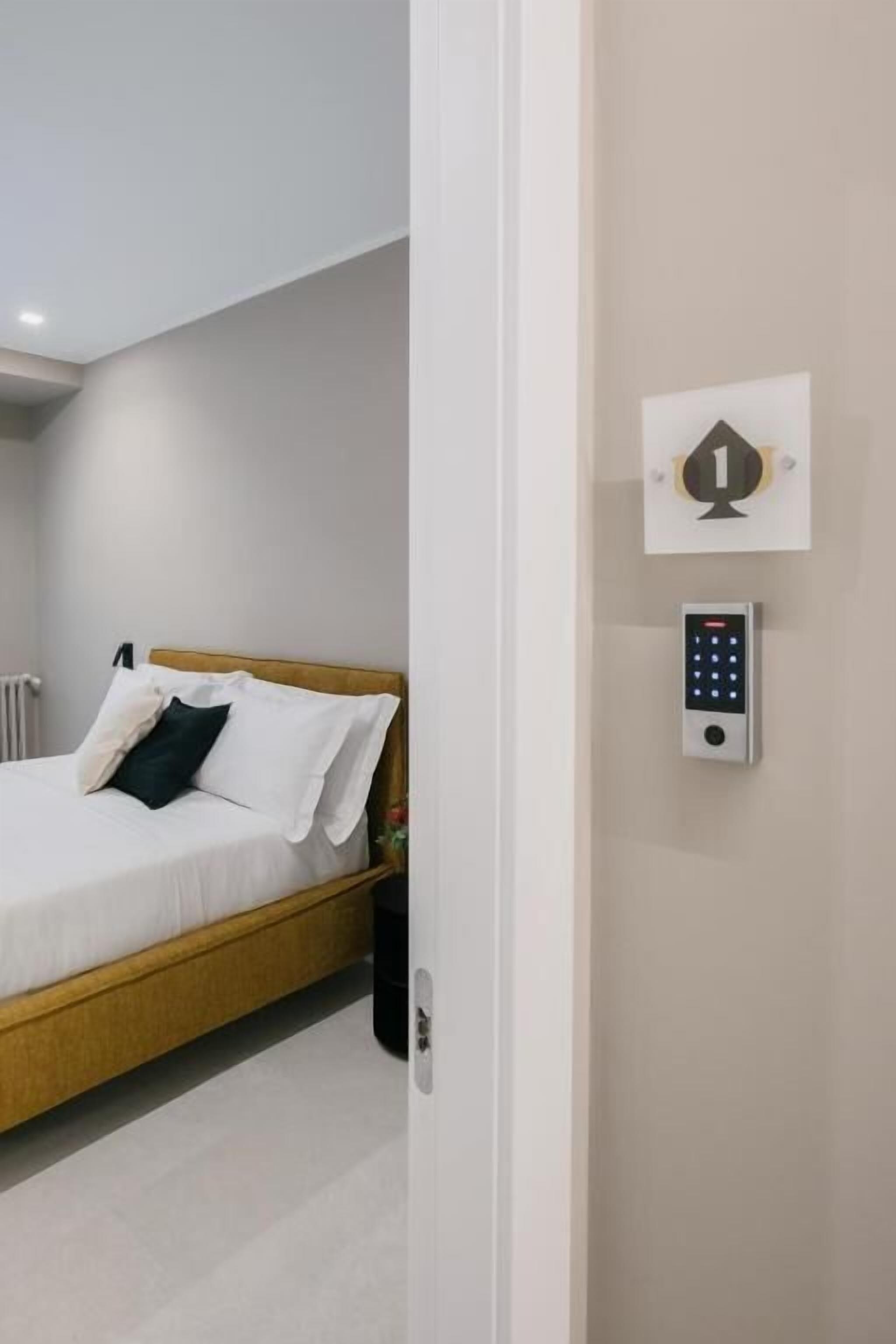 Un dormitorio moderno con una cama de madera, ropa de cama blanca, un panel de control en la pared y una puerta con manija.