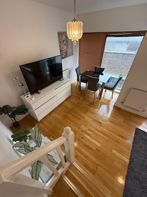 Ein modernes Wohnzimmer mit Flachbildfernseher, einer Kristallleuchtre, einem Esstisch mit Stühlen und einer Treppe.