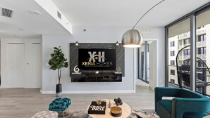 Ein modernes Wohnzimmer mit einem großen, an der Wand befestigten Fernseher, einem Topfpflanzen und einem salbeengrünem Sofa.