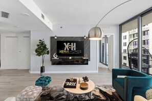 A modern living room with a large TV mounted on the wall, a potted plant, and a teal sofa. - Highrise  2-bedroom condo in The Heart of Brickell (Miami)