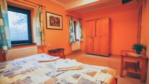 Ein Schlafzimmer mit einem Bett, einem Holzschrank, einem Fenster mit Vorhängen, einer Heizung und einem kleinen Tisch mit Pflanze.