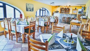 Ein Restaurant mit mehreren Tischen und Stühlen, einer Bar und Blick durch große Fenster.