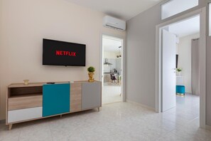A modern living room with a TV displaying 'NETFLIX,' a wooden cabinet, and a doorway leading to another room.