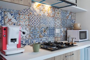 Une cuisine équipée d’une machine à café, d’une tasse, d’une cuisinière à gaz et d’un four à micro-ondes.
