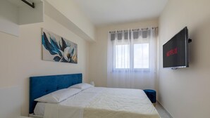 Une chambre à coucher avec un lit, un tableau, une télévision et une fenêtre avec des rideaux.