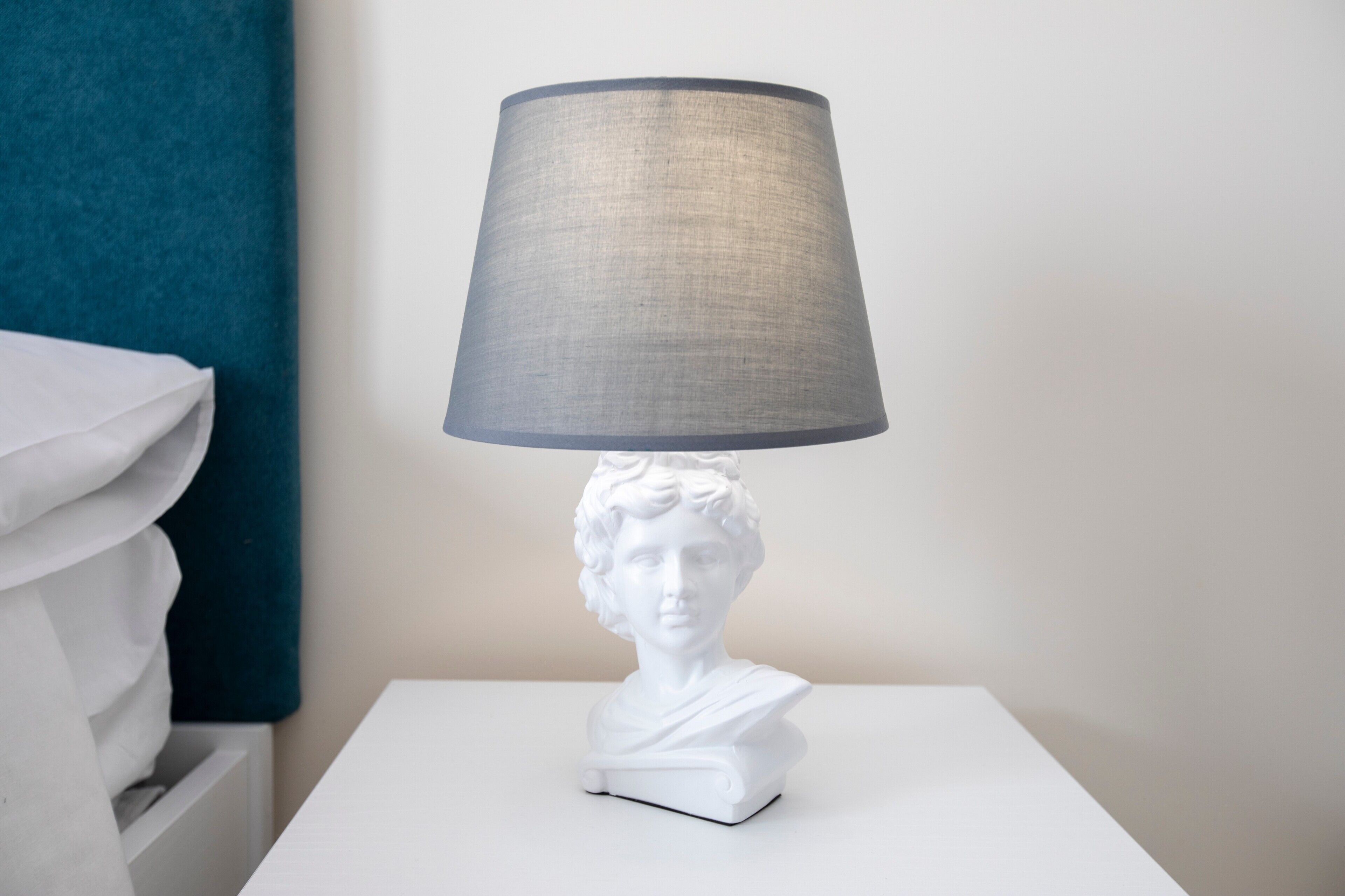 Eine weiße Büstenstatue auf einem weißen Tisch mit einem grauen Lampenschirm.