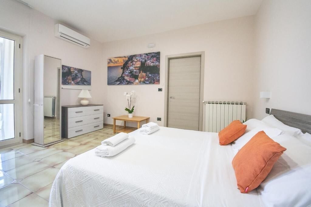 Un dormitorio con cama, almohadas, cómoda, espejo, radiador y obras de arte en la pared.