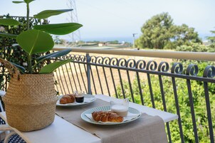 Un balcón con una mesa lista para el desayuno, una planta en maceta y vista al mar.
