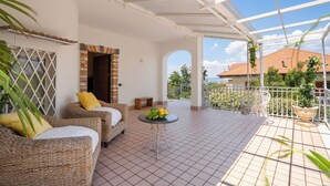 Un espacio al aire libre cubierto con muebles de mimbre, una mesita con flores y vista a un edificio al fondo.