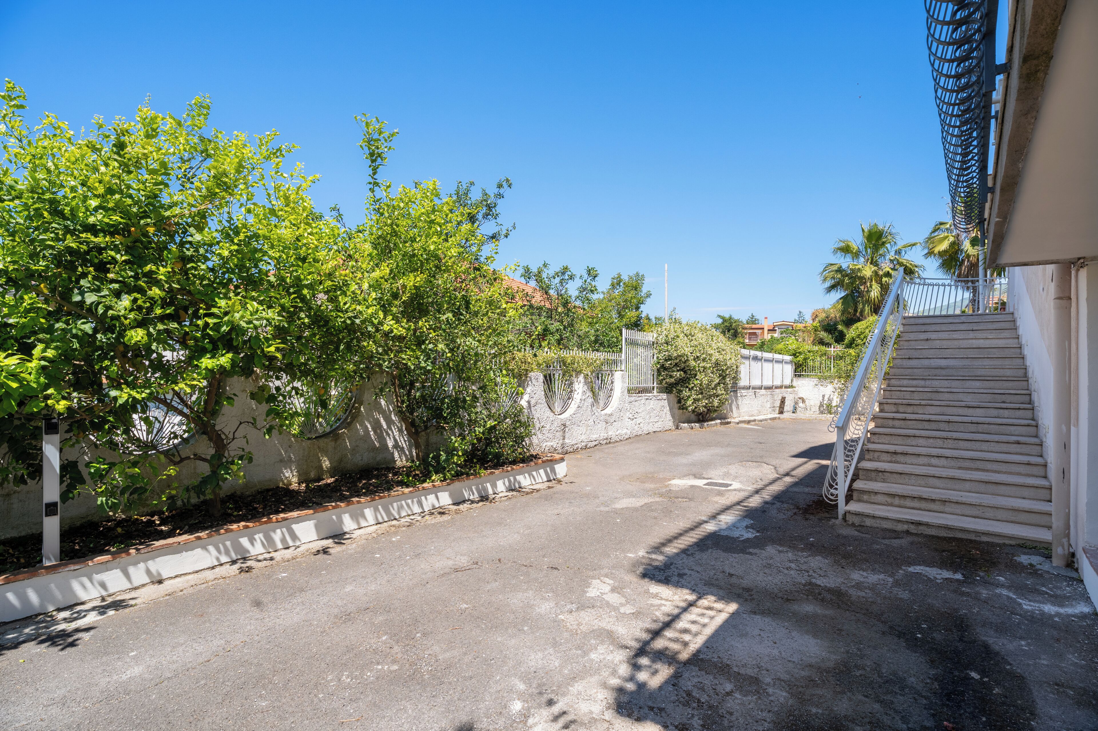 A residential street with a staircase leading to a building, surrounded by greenery and a clear sky.