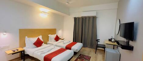 A hotel room with two beds, a desk, a TV, and a small kitchenette.