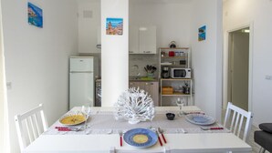 A dining area with a white table set for four, a white chair on each side, and a white decorative tree centerpiece. - VivimiHome-Casa Tiberio (Conca dei Marini)