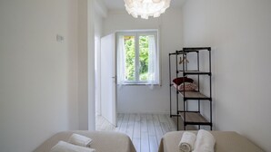 A room with a bed, a shelf with folded towels, a hanging light fixture, and a window with curtains. - VivimiHome-Casa Tiberio (Conca dei Marini)
