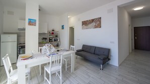 A modern kitchen with white cabinets, a dining table set for two, and a grey sofa in the living area. - VivimiHome-Casa Tiberio (Conca dei Marini)