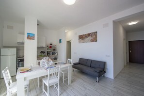 Une cuisine moderne avec des meubles blancs, une table à manger dressée pour deux personnes et un canapé gris dans l’espace salon.