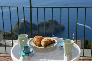 Ett bord med croissanter och koppar på en balkong med utsikt över havet.
