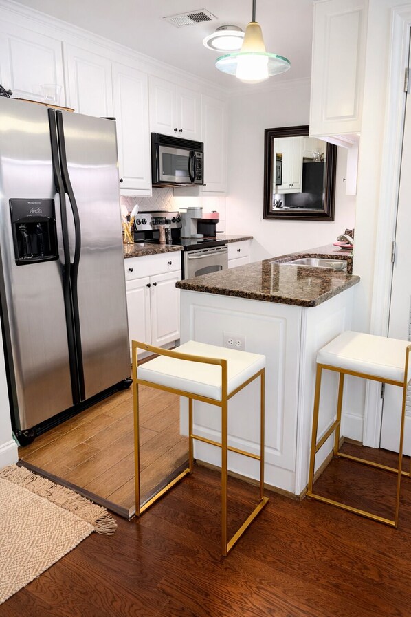 Una cocina moderna con muebles blancos, electrodomésticos de acero inoxidable, una encimera de granito y dos taburetes de bar.