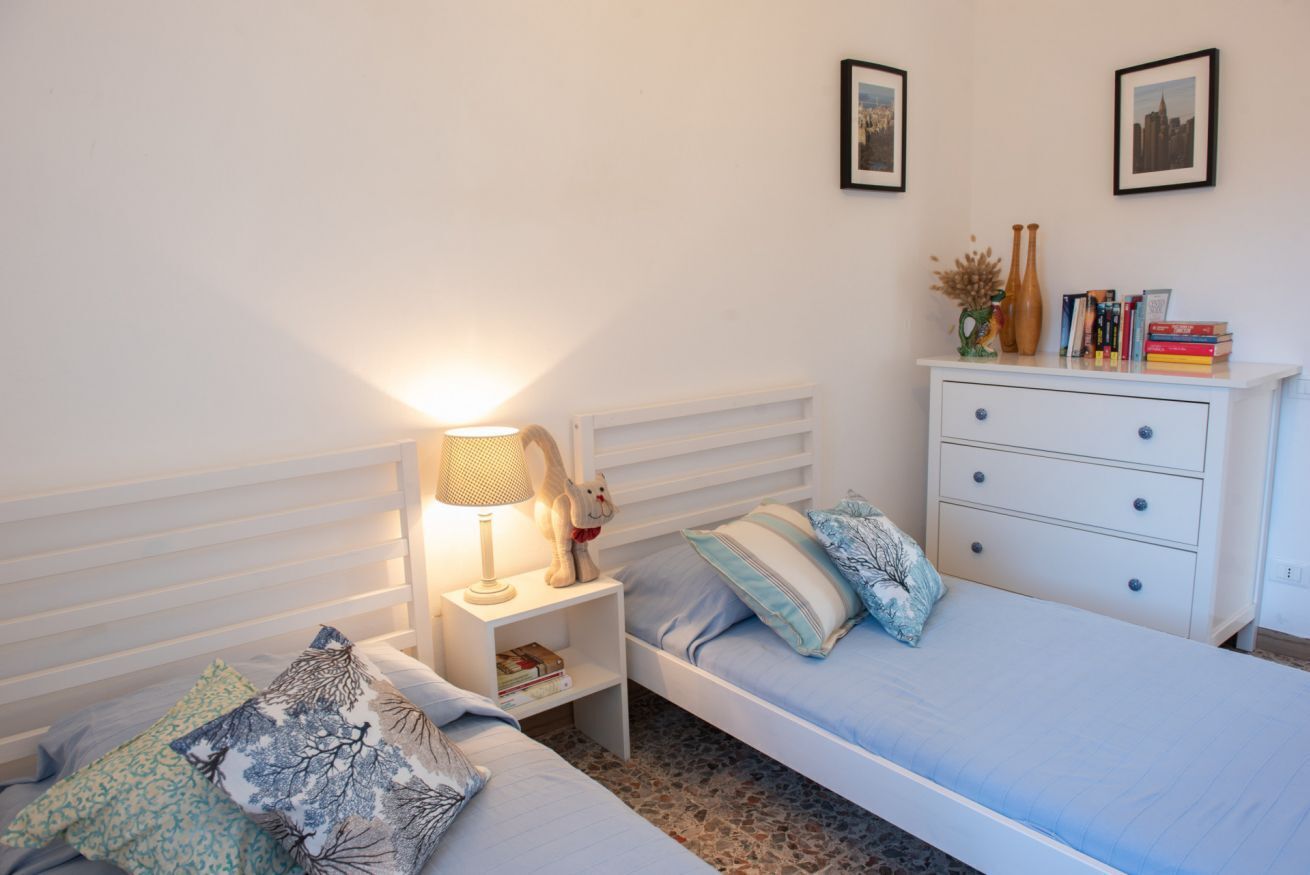 Une chambre avec un lit simple, une table de chevet avec une lampe, une commode et deux tableaux encadrés au mur.