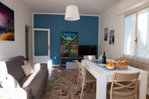 A modern living room with a sofa, dining table, and artwork on the walls. - Casa Tirreno: Spacious Seaside Apartment with Private Parking & Balcony (San Vincenzo)
