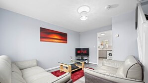 Una sala de estar moderna con un sofá, una mesa de centro de vidrio, una alfombra roja y un televisor que muestra 'NETFLIX'.