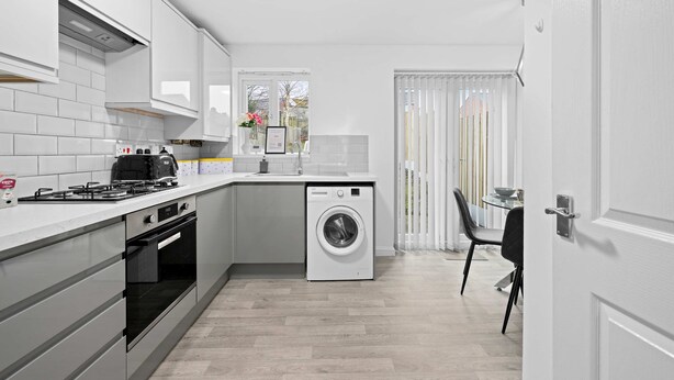 Una cocina moderna con armarios blancos, horno empotrado, lavadora y comedor con mesa y sillas.