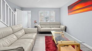 Una sala de estar moderna con un sofá color beige, una mesa de centro de cristal y una alfombra roja.