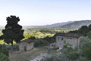 Ein Gebäude aus Stein mit einem Ziegeldach, umgeben von Grün und Blick auf ein Tal.