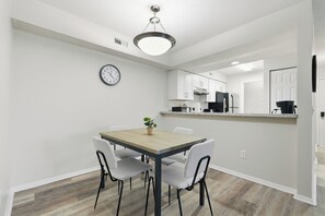 Cozinha moderna com armários brancos, uma mesa de jantar de madeira e um relógio na parede.