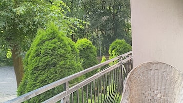A balcony with a wicker chair, metal railing, and lush greenery in the background.