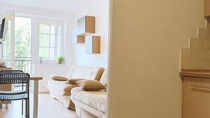 Una sala de estar moderna con un sofá, una mesa de comedor y una silla. Se aprecia una zona de cocina con armarios y una encimera.