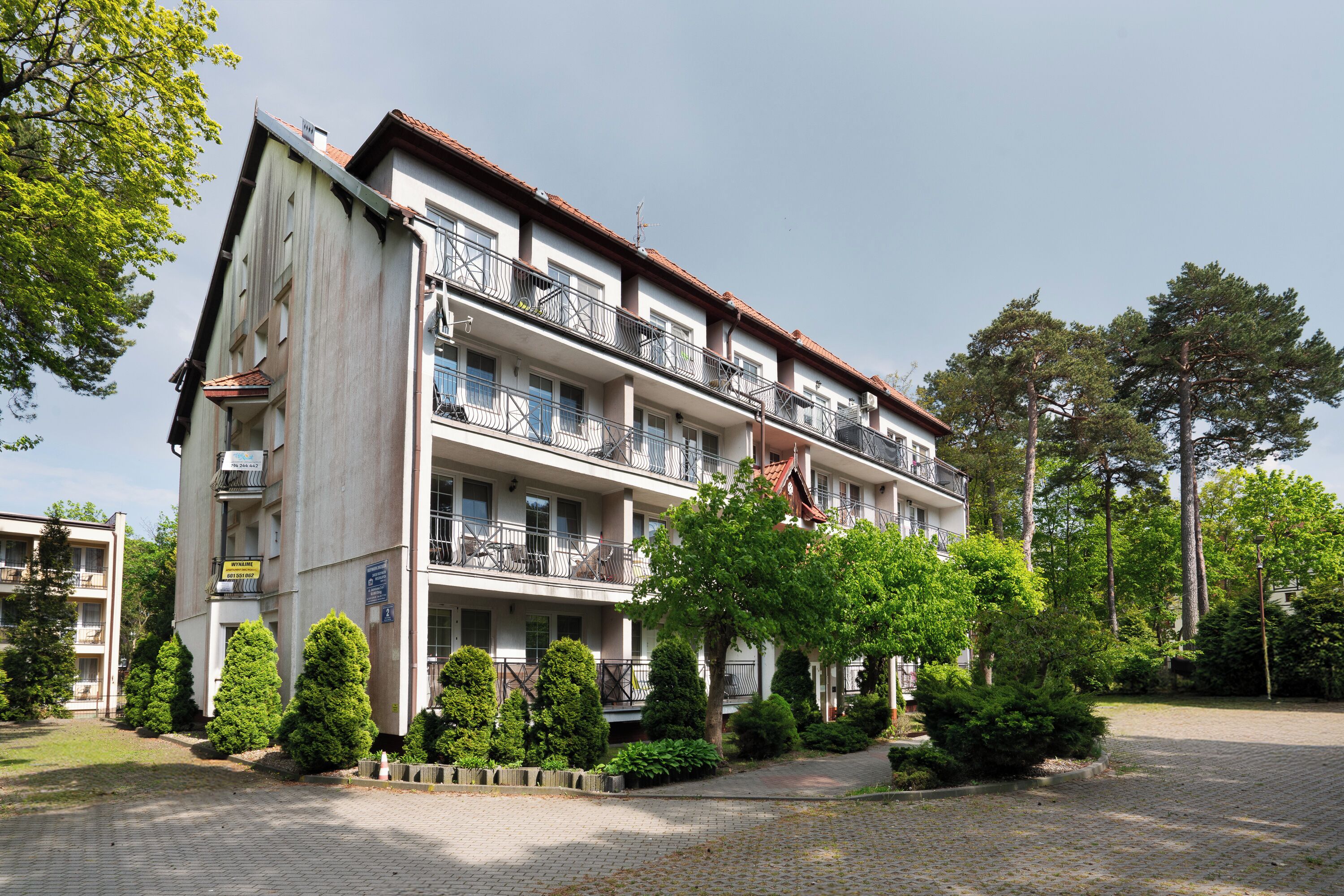A multi-story hotel with balconies, a paved courtyard, and surrounding greenery.