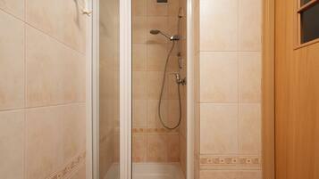 A walk-in shower with beige tiles, a handheld showerhead, and a handheld faucet.