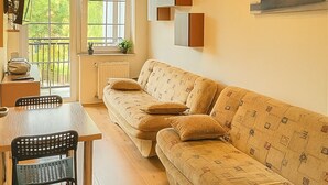 Una sala de estar acogedora con un sofá, una mesa de comedor y sillas. Se ve una ventana con vistas a zonas verdes.