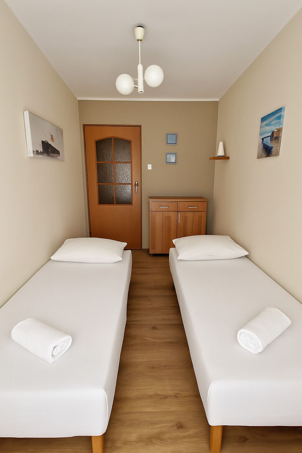 Quarto com duas camas de solteiro, um guarda-roupa de madeira, uma porta com painéis de vidro e um lustre.