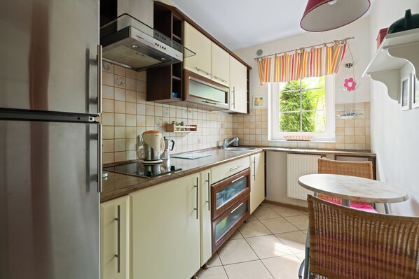 A kitchen with a refrigerator, oven, and sink. There is a window with curtains and a table with chairs. - HoliApart Zeromskiego 150m beach (Krynica Morska)