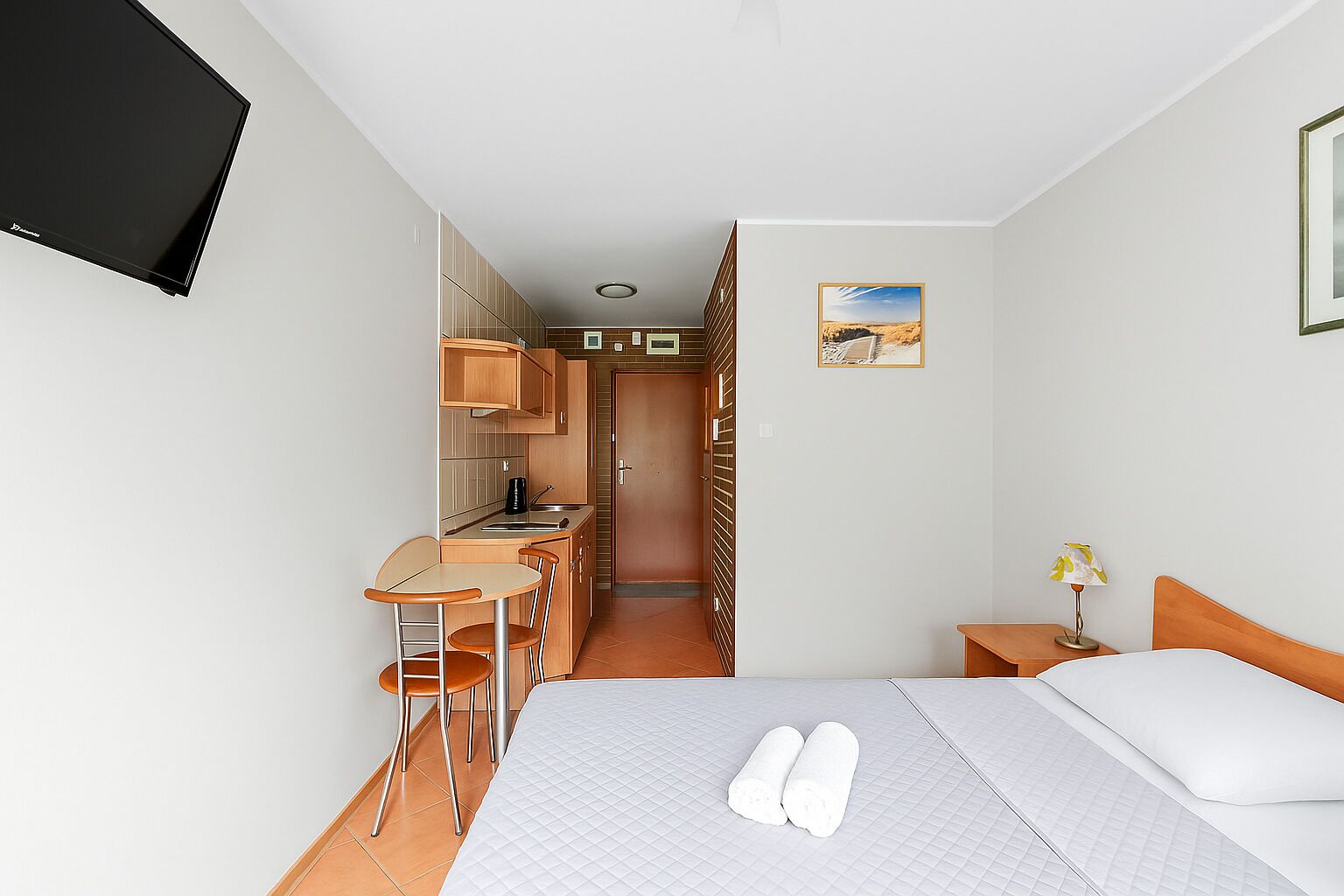 Een hotelkamer met een bed, een klein bureau met stoel, een kitchenette en een badkamer.