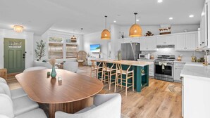 Eine moderne Küche mit weißen Schränken, einem Holztisch und Pendelleuchten.
